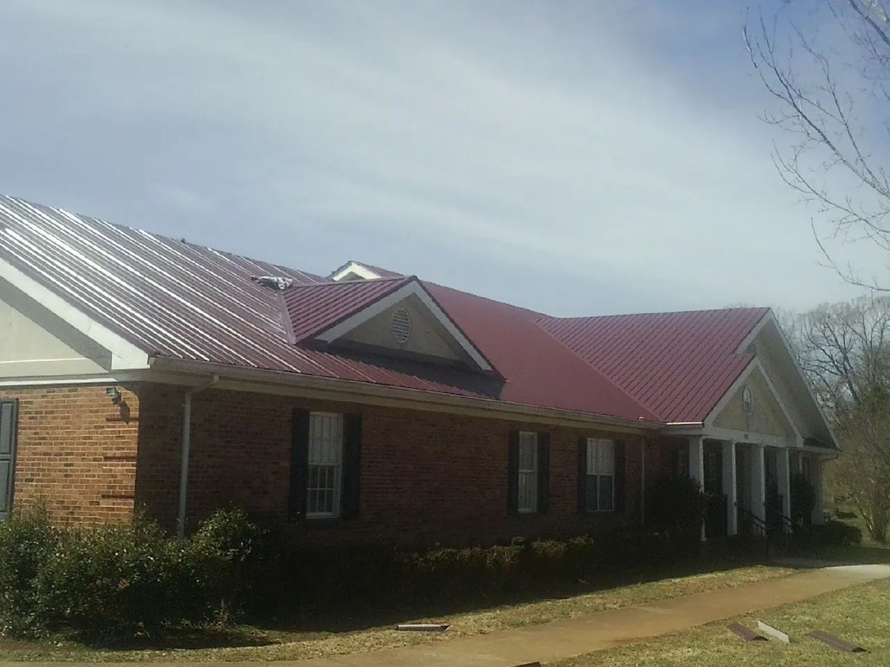 Red metal roof with gabled entries on a long brick building, from a Hail Damage Roof Repair job in Rockbridge Baths
