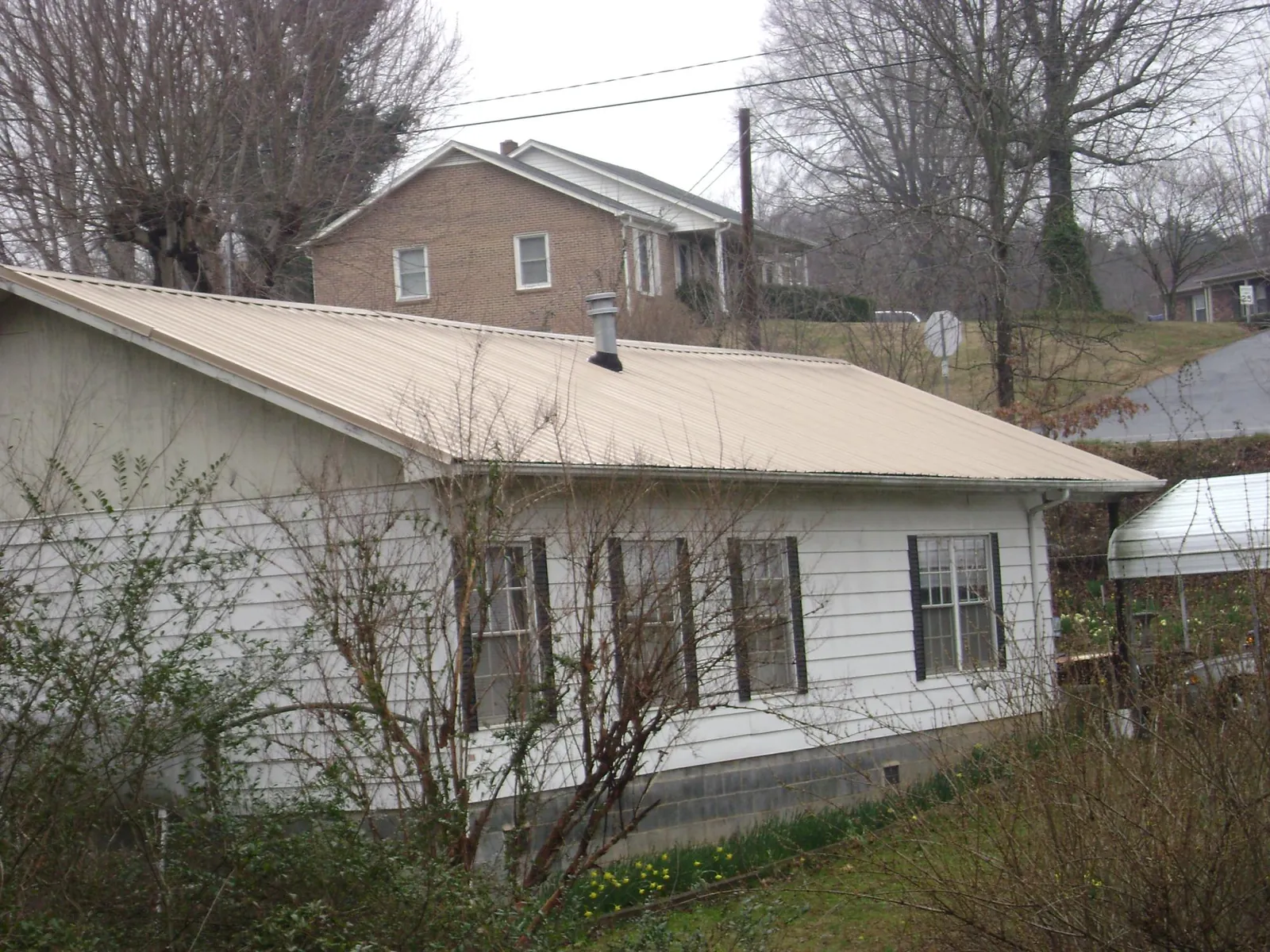 Tan metal roof on a white sided house set into a hillside — Commercial Roofing by Roofing Brothers in Rockbridge Baths
