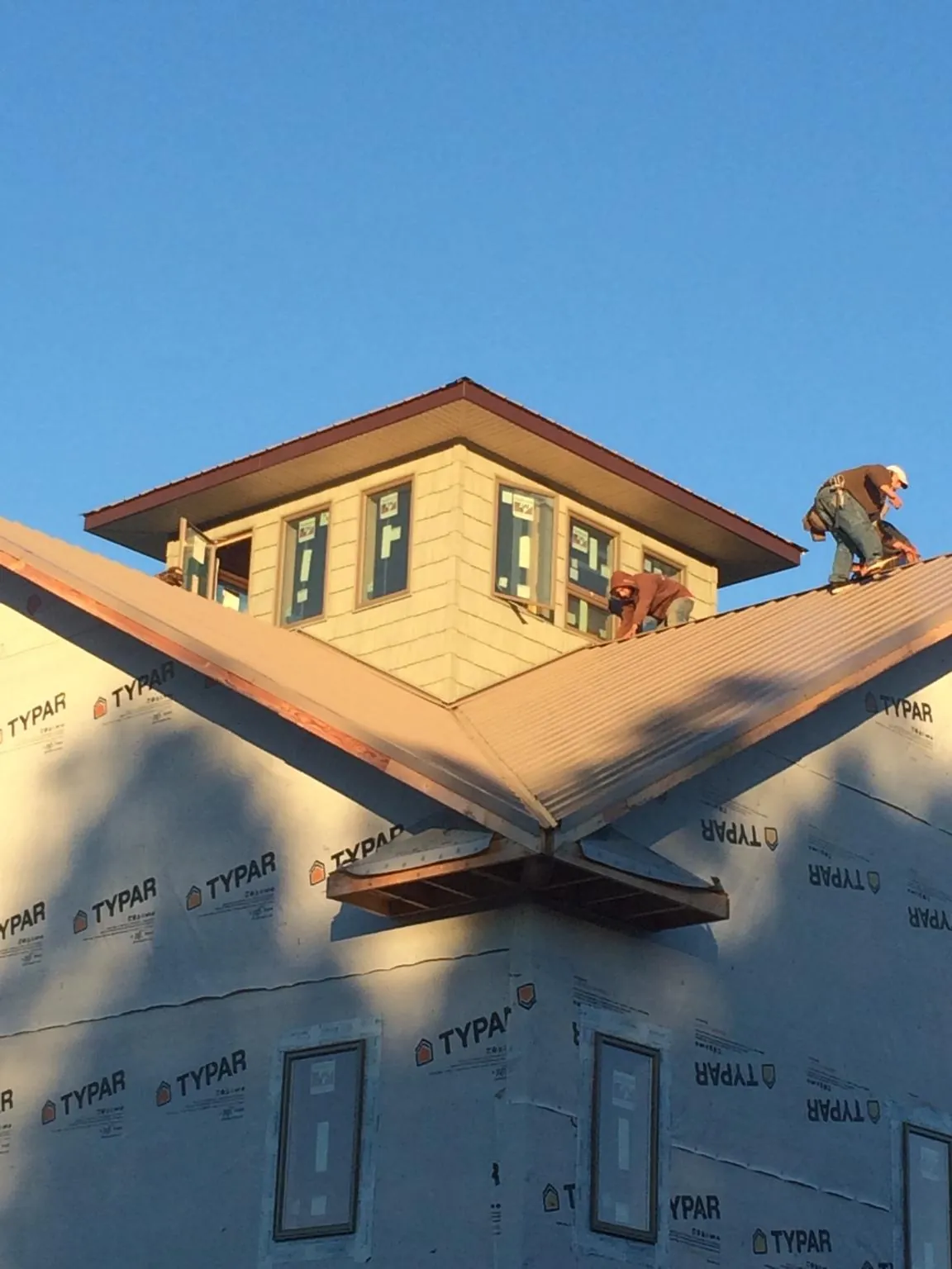 Roofers working around a rooftop cupola on a new metal roof at sunset — Roof Waterproofing in Rockbridge Baths by Roofing Brothers
